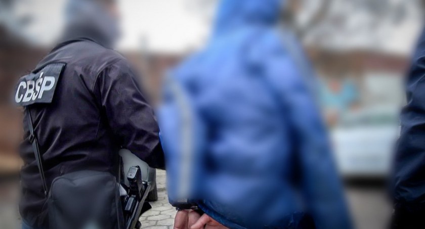 Zdjęcie policjanta z CBŚP prowadzącego podejrzanego/ podlaska.policja.gov.pl
