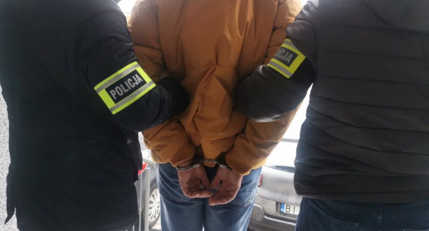 Zdjęcie zatrzymanego mężczyzny w kajdankach prowadzonego przez policjanta/ podlaska.policja.gov.pl