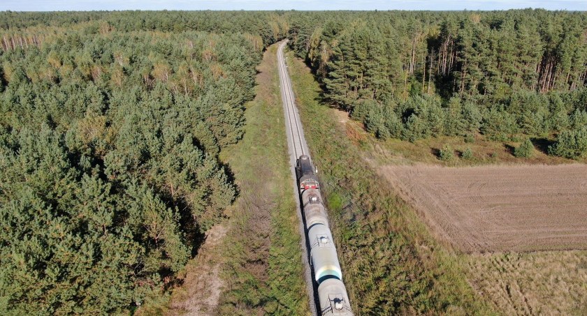 Zdjęcie torów kolejowych i pociągu w terenie z zielenią/ PKP PLK