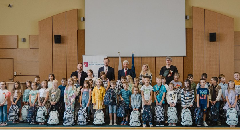 Zdjęcie dzieci z wyprawkami szkolnymi raz przedstawicieli urzędu wojewódzkiego/ PUW