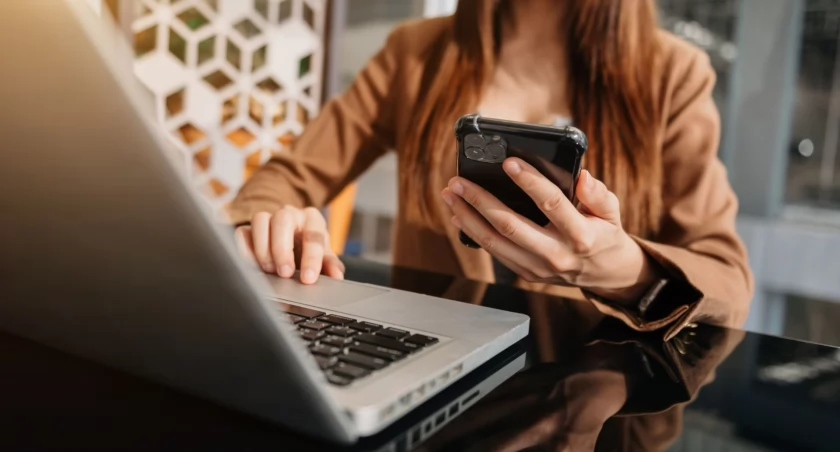 Zdjęcie kobiety z telefonem w ręce przy laptopie