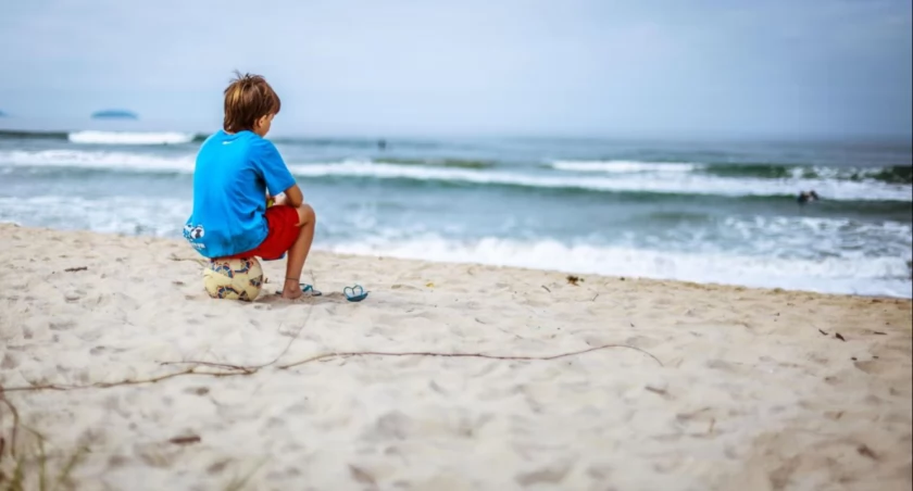 Zdjęcie dziecka siedzącego na piłce na plaży