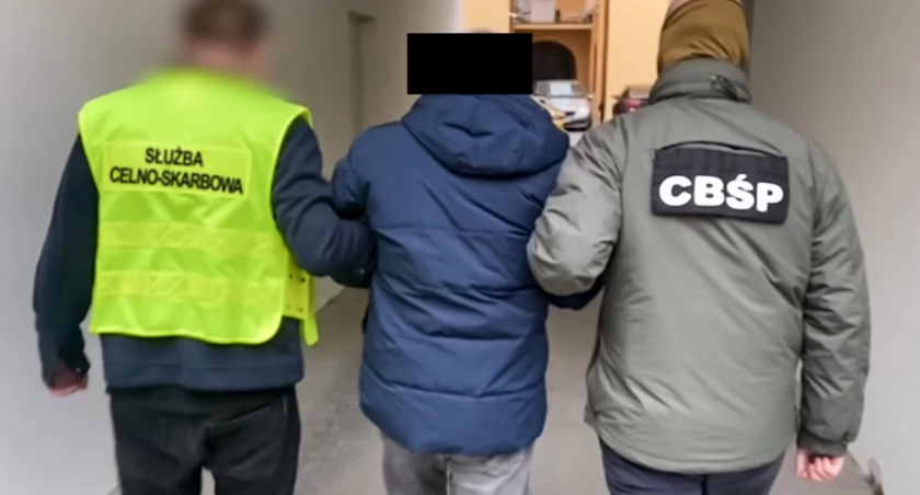 Zdjęcie funkcjonariusza KAS i CBŚP prowadzących zatrzymanego mężczyznę/ CBŚP