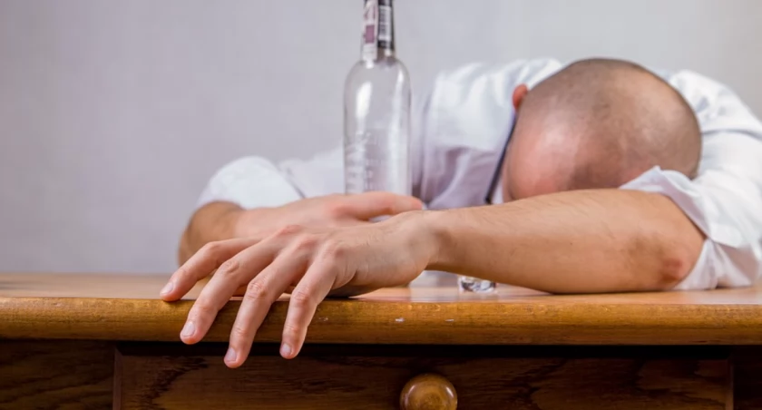 Zdjęcie mężczyzny śpiącego przy pustej butelce/ Pixabay.com