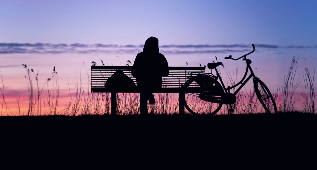 Zdjęcie samotnej osoby siedzącej na ławce przy stojącym rowerze/ Pixabay.com