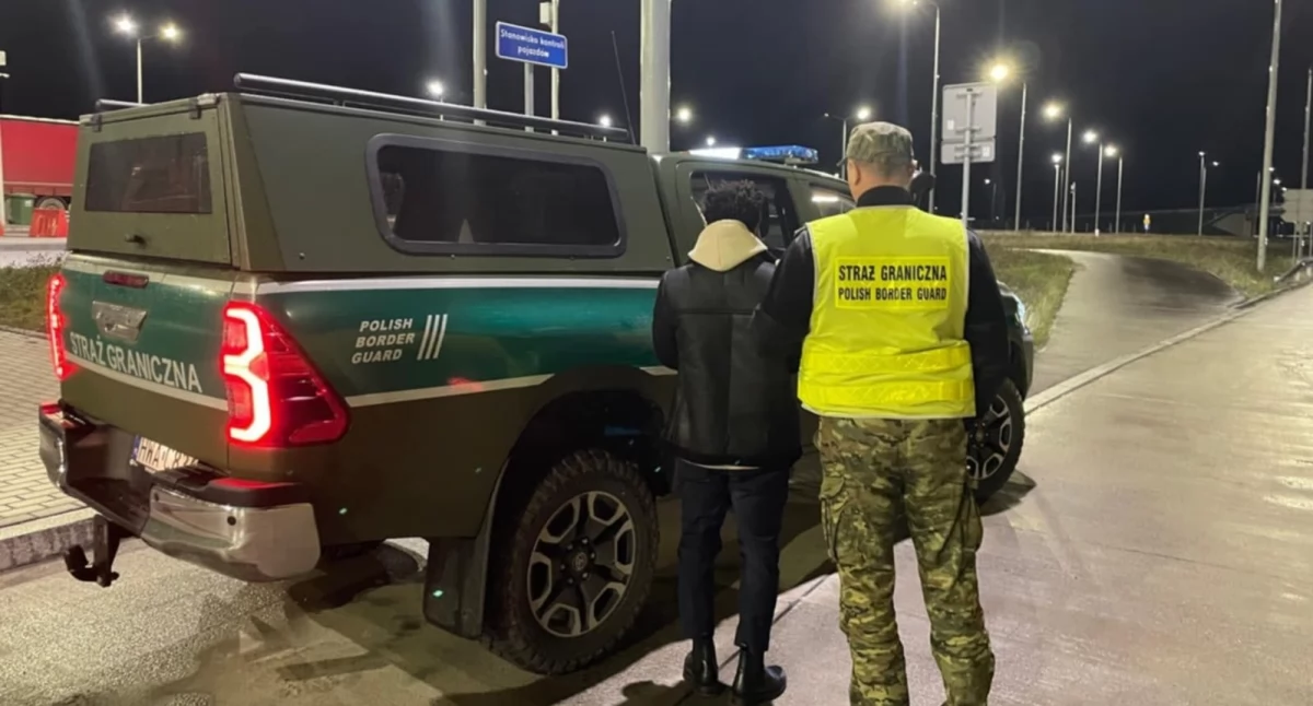 Zdjęcie strażnika granicznego przy pojeździe służbowym z zatrzymanym nielegalnym migrantem/ SG