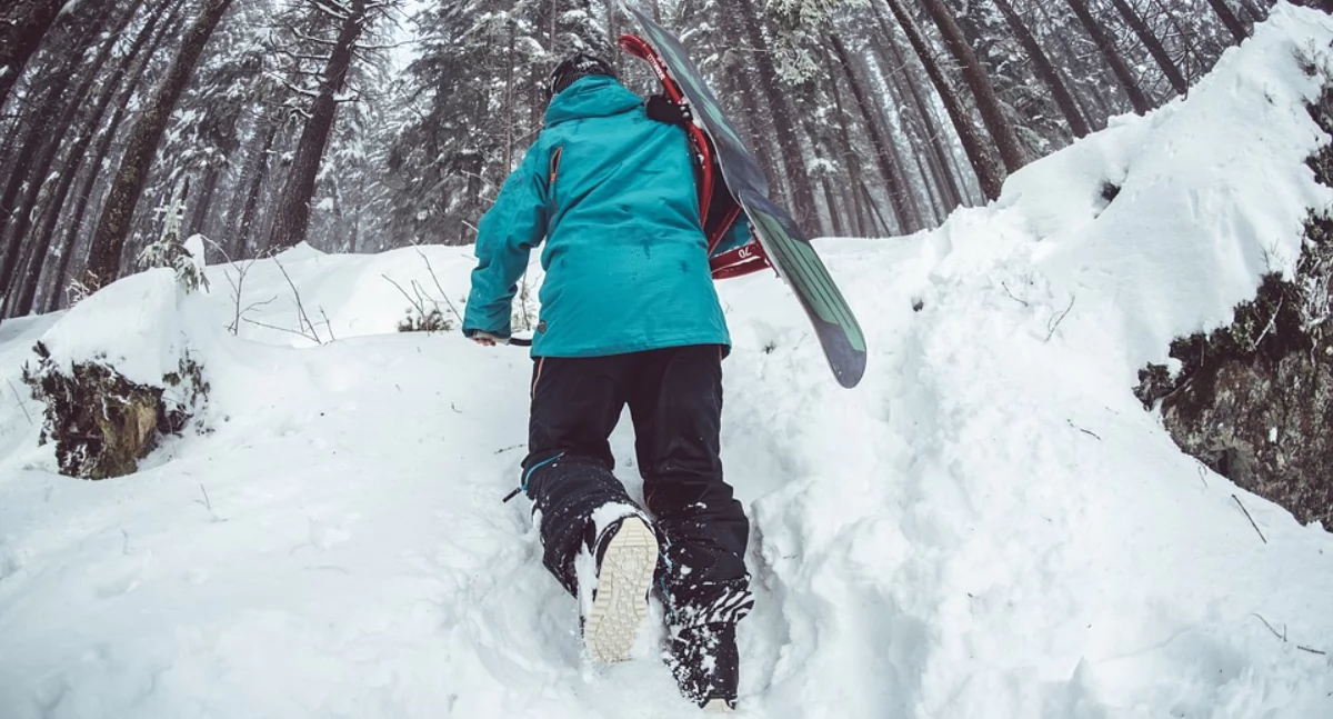 Zdjęcie chłopca idącego po śniegu z deską snowboardową/ Pixabay.com