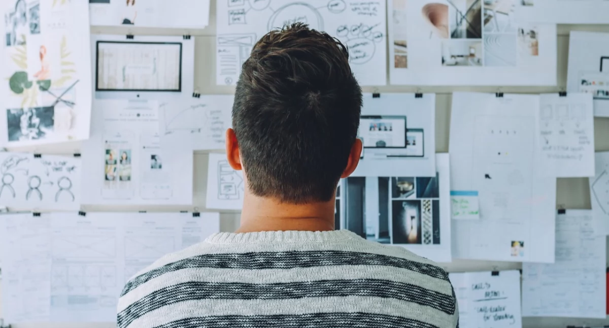 Zdjęcie mężczyzny siedzącego przed tablicą z przyczepionymi kartkami/ Pixabay.com
