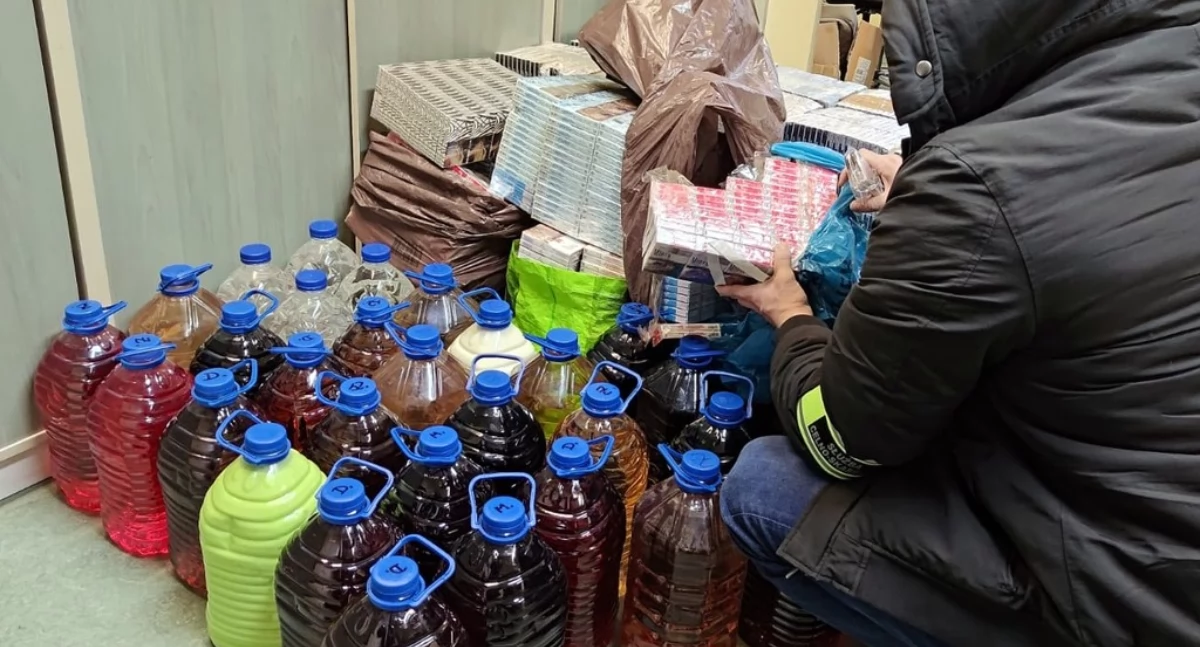 Zdjęcie funkcjonariusza KAS przy zarekwirowanym alkoholu i papierosach/ KAS